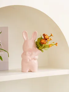 Primer plano de un lindo florero de conejo de cerámica rosa con flores naranjas en estante.