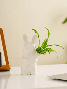 Primer plano de florero de conejo de cerámica blanca con planta verde, decorativo.