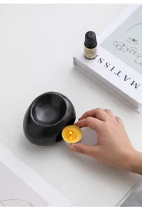 Primo piano di bruciatore di oli essenziali in ceramica nera con candela accesa.