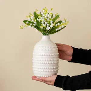 Vue détaillée d'un vase en céramique blanche texturé de perles et de fleurs de muguet.