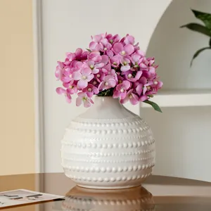Gros plan d'un vase en céramique blanche texturée avec composition florale artificielle rose.