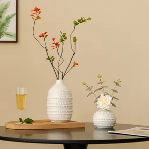 Gros plan de vases en céramique blanche nordique texturés de perles, sur une table sombre.