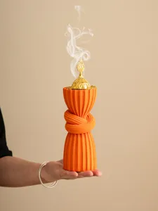 Arabic style orange resin incense burner close-up detail with golden lid and rising smoke.