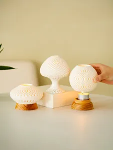 Detail view of white 3D printed hollow candle holders with wooden bases, creating warm lighting.