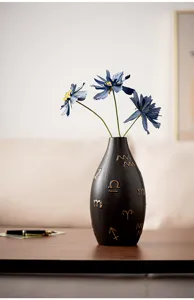 Close-up detail of a modern black ceramic vase featuring elegant gold zodiac symbols and blue flowers.