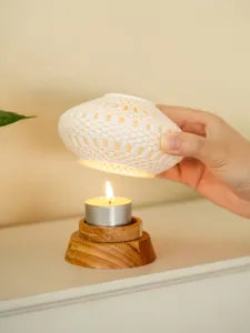 Detailed view of white hollow 3D printed ceramic candle holder shade with wooden base and tea light.