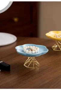Detailed shot of a ceramic jewelry tray with a gold metal stand on a wooden desk.