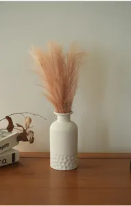 Détail de vase en céramique blanche nordique, design texturé en bas et décor d'herbe séchée.