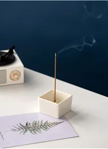 Detailed shot of a minimalist square white ceramic incense burner with burning stick and smoke.