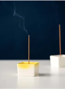 Detail view of a minimalist square ceramic incense holder in white and yellow gradient.