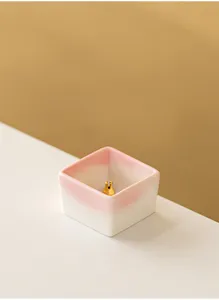 Close-up of minimalist square ceramic incense holder with pink gradient and gold holder.