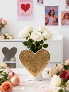 Detail shot of white ceramic heart vase with gold texture and fresh white roses on table.