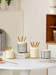 Ceramic tableware storage jar with golden metal frame and spoons, clean desktop organizing display detail.