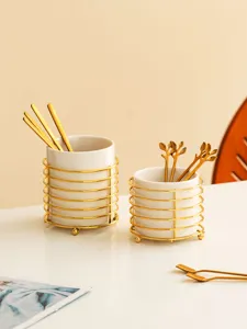 Close-up detail of ceramic cutlery storage holder with gold iron stand and spoons.