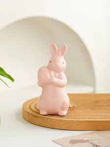 Detailed close-up of a cute pink ceramic Easter bunny figurine holding an egg for home decor.