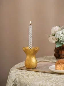 Close-up detail shot of a gold resin flower candle holder with a burning twisted candle on table.