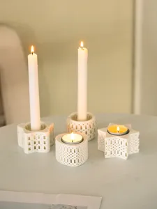 Detailansicht von weißen, hohlen Kerzenhaltern aus Keramik mit brennenden Kerzen.