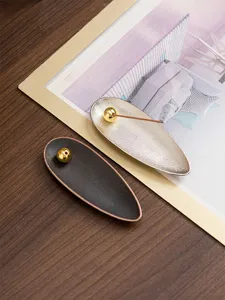 Close-up detail of modern creative willow leaf incense holder with golden bead design on wooden desktop scene.