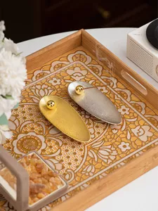 Detail shot of modern willow leaf incense holder with gold and silver finish on wooden tray.