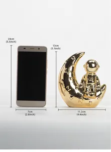 Gold ceramic astronaut moon ornament detail view showing size comparison with phone decor.