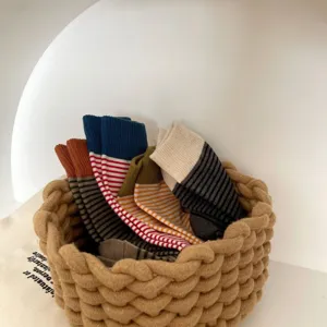 Detailed view of women's autumn winter striped mid-tube socks with colorful ribbed cuffs in woven basket.