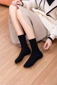 Close-up detail shot of classic black ribbed mid-calf socks worn by a model on wooden floor.