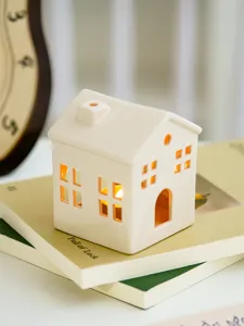 Ceramic house candle holder detail, modern minimalist design with warm glowing light windows.