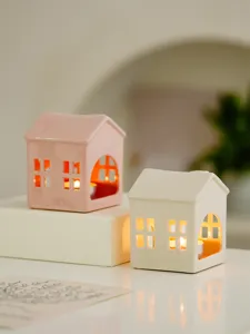 Detailed view of ceramic house candle holders, featuring hollow windows and warm glowing light for home.