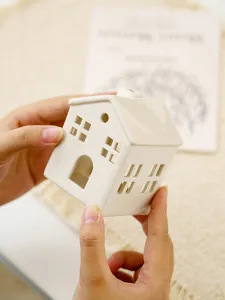 Detailed view of white ceramic house candle holder, hollow design for cozy home table decor.