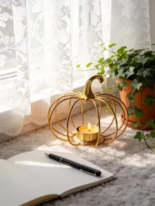 Golden iron wire pumpkin tealight candle holder with burning candle, cozy desktop decor.