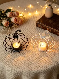 Close-up detail of metal pumpkin candle holders on a cozy knitted table setting with warm lights.
