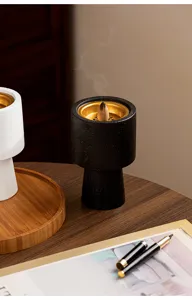 Detail shot of modern black incense burner with burning cone smoke on wooden desk setup.
