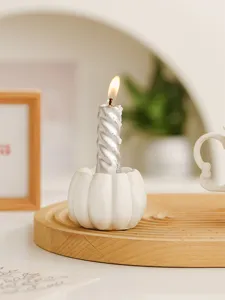 Detail shot of white resin pumpkin candle holder with silver spiral candle on wooden tray.
