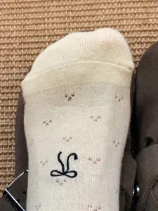 Close-up detail of cream ballet-core mid-tube socks with cute jacquard flowers and black bow.