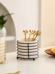Detailed view of ceramic utensil holder with elegant gold leaf spoons on white tabletop.
