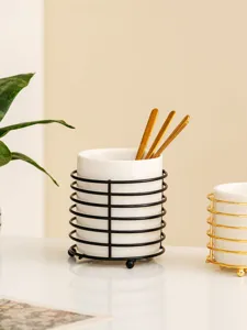 Close-up view of a ceramic storage jar with a black metal wire frame and golden spoons inside.