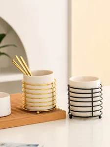 Close-up of modern white ceramic utensil holder with elegant gold and black metal wire frames.