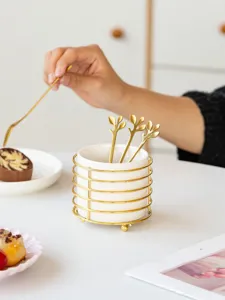 Ceramic cutlery storage holder with gold metal rack and leaf spoons for desktop organization.