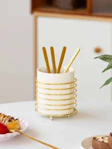 Close-up of ceramic cutlery holder with gold wire frame, elegant tabletop kitchen storage detail.