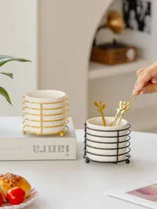Ceramic tableware storage jar with metal rack and golden spoons for desktop organization.