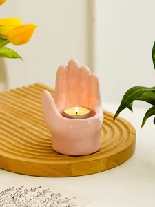 Close-up of a cute pink ceramic hand candle holder with tealight on wooden tray for decor.