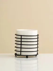 Close up of white ceramic utensil holder with black metal wire stand for kitchen table storage.