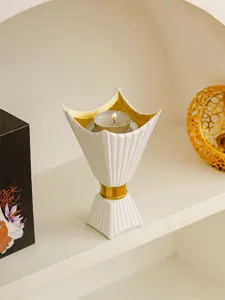 Close-up of white and gold geometric candle holder with burning tealight on shelf display.