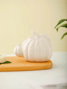 Close-up of modern ceramic pumpkin ornament on wooden tray, elegant tabletop decor detail.