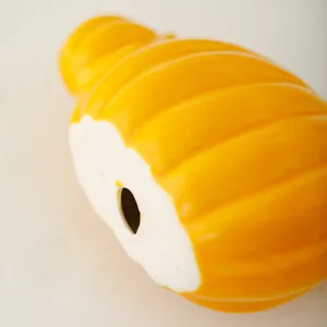 Close-up detail shot of a bright yellow ceramic pumpkin ornament showing smooth glossy finish.