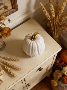 Detailed shot of a white ceramic pumpkin decor piece with gold stem, on a vintage styled tabletop.