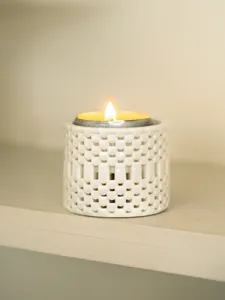 Detailansicht des weißen Keramik-Teelichthalters mit hohlem Design und brennender Kerze.