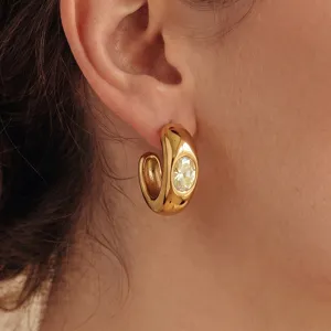 Detalle en primer plano de pendiente de aro dorado con piedra de cristal amarillo.