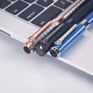 Close-up detail shot of three premium metal ballpoint pens in multi colors on laptop surface.