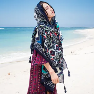 Detail view of a bohemian floral print cotton linen scarf shawl with handmade tassels on beach.
